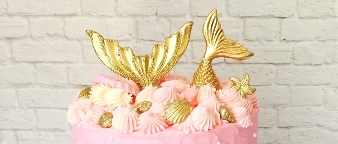 A pink cake with gold decorations on top of it.