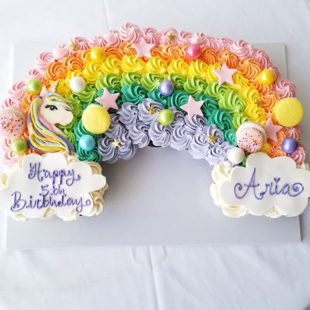 A rainbow cake with stars and clouds on top.