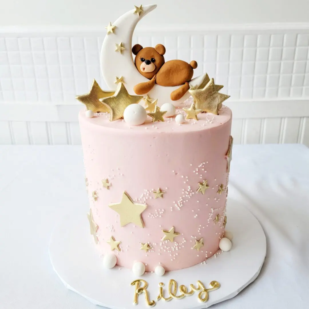 A pink cake with bear and moon toppers