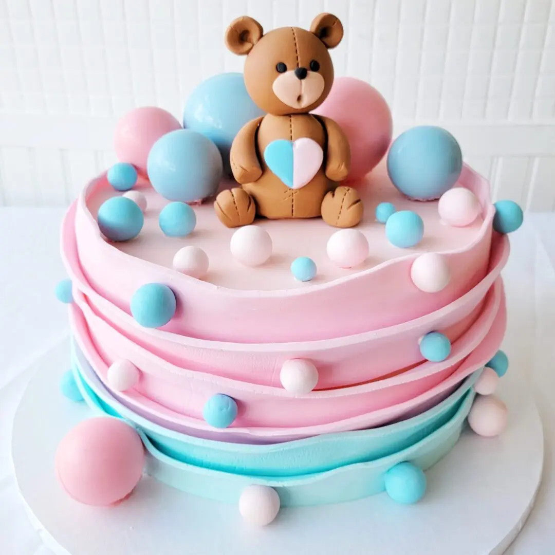 A pink and blue cake with a bear topper