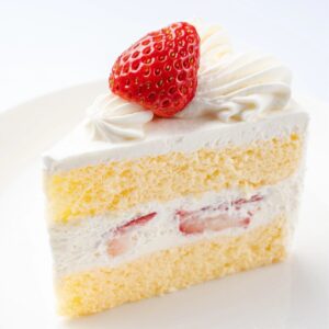 A piece of cake with white frosting and strawberry on top.