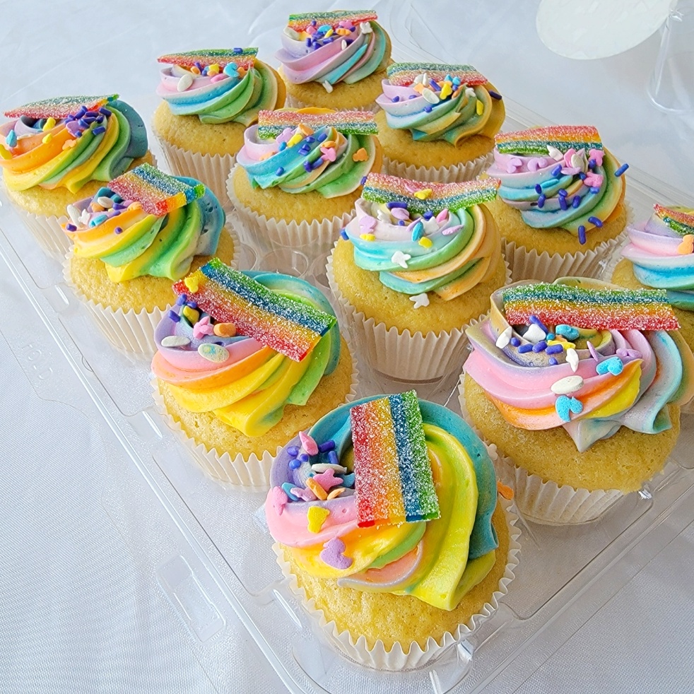 A tray of cupcakes with rainbow frosting and decorations.